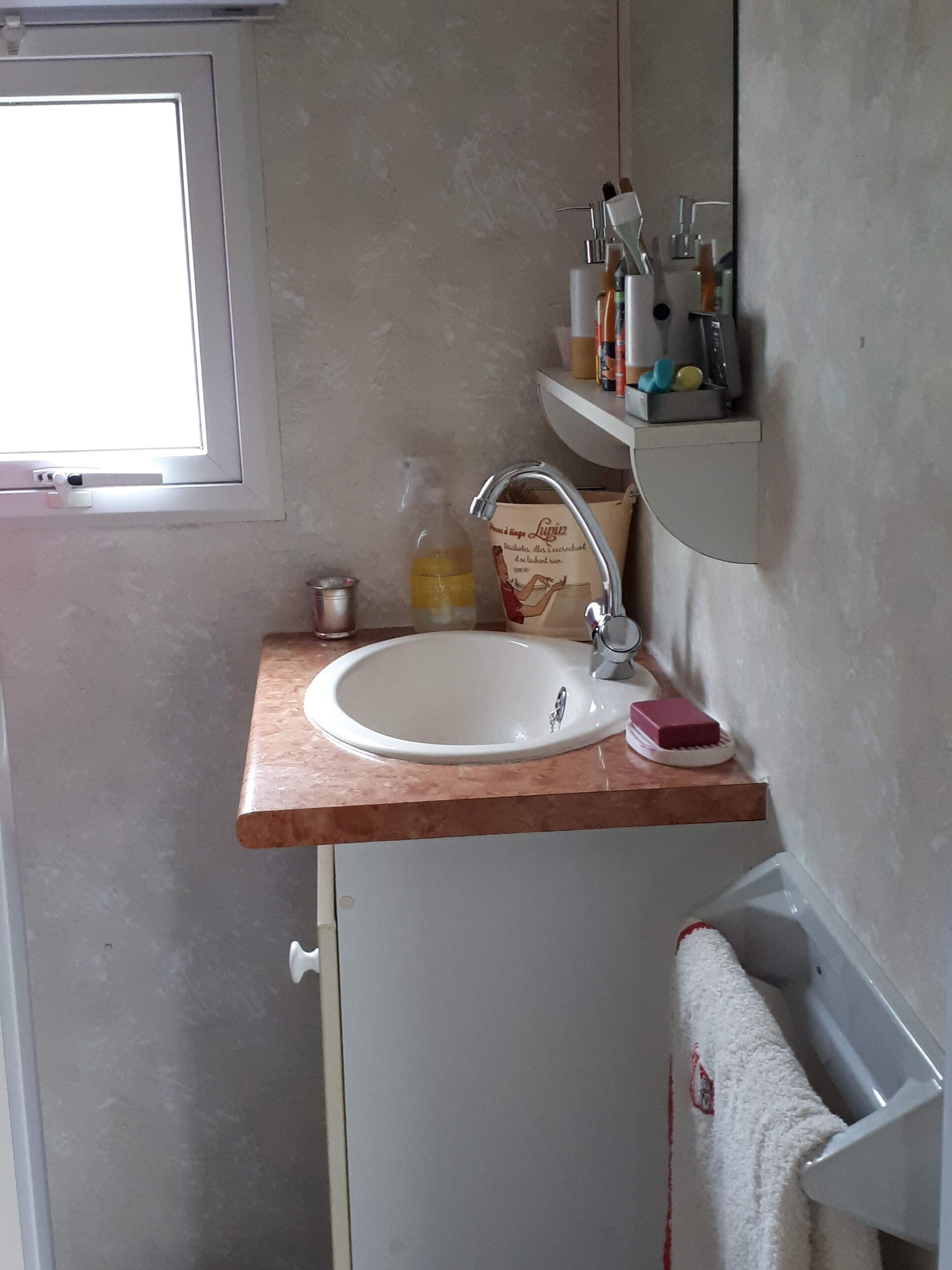 A bathroom with a white sink, a mirror, a towel rack, and a shelf with toiletries.