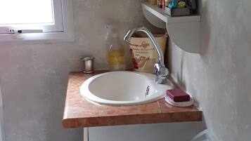 A bathroom with a white sink, a mirror, a towel rack, and a shelf with toiletries.