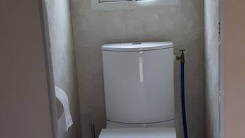 Un baño pequeño y estrecho con un inodoro, una ventana encima y baldosas de piso estampadas.