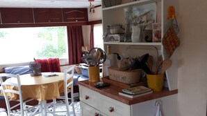 A kitchen with a patterned floor, a dining table with chairs, a white cabinet with drawers, and a window with curtains.