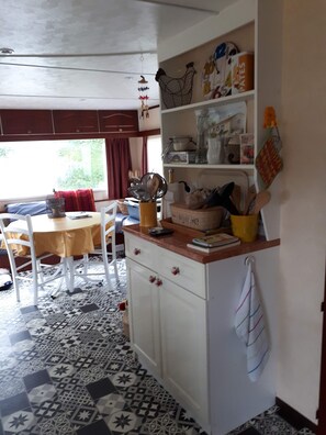 A kitchen with a patterned floor, a dining table with chairs, a white cabinet with drawers, and a window with curtains.