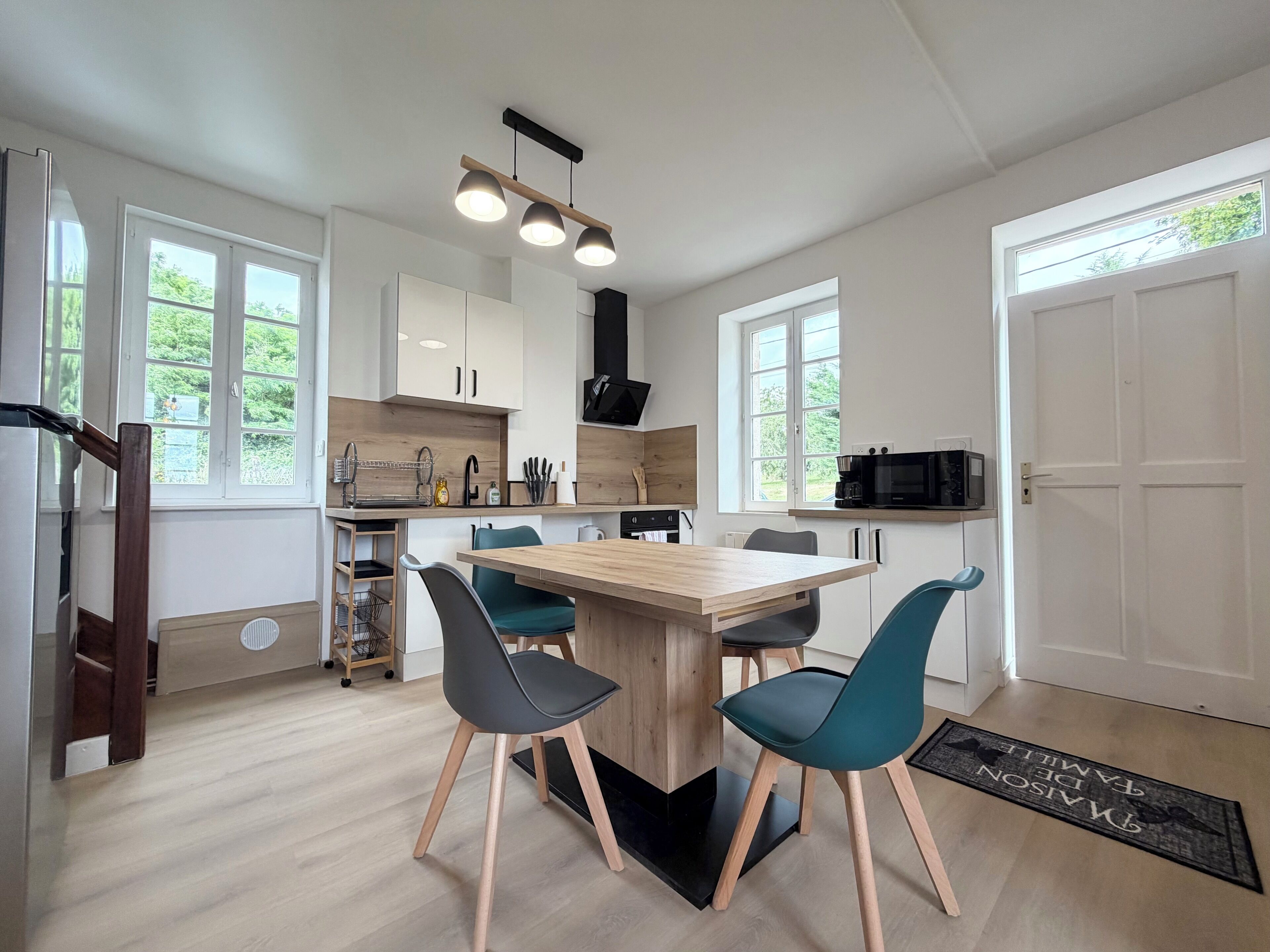 A modern kitchen with a central island, white cabinets, and a dining area with teal chairs.. Le Cocoonie - Comfort, charm and relaxation