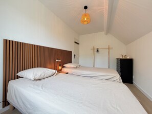 Une chambre avec deux lits, une tête de lit en bois, un luminaire suspendu et une armoire.