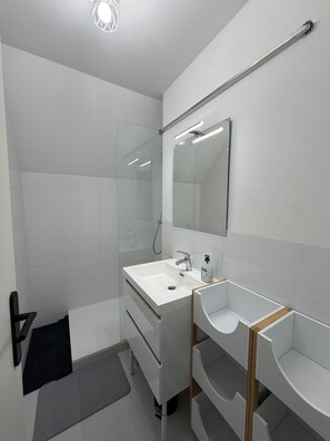 Une salle de bain moderne avec une douche à parois de verre, un lavabo blanc avec un miroir au-dessus et un meuble-lavabo en bois.