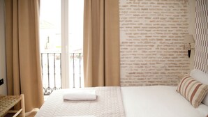Una camera d'albergo con un letto, tende, una finestra vista, un muro a mattoni e una lampada.