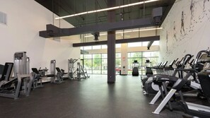 Ein Fitnessstudio mit verschiedenen Trainingsgeräten, großen Fenstern und Blick ins Freie.