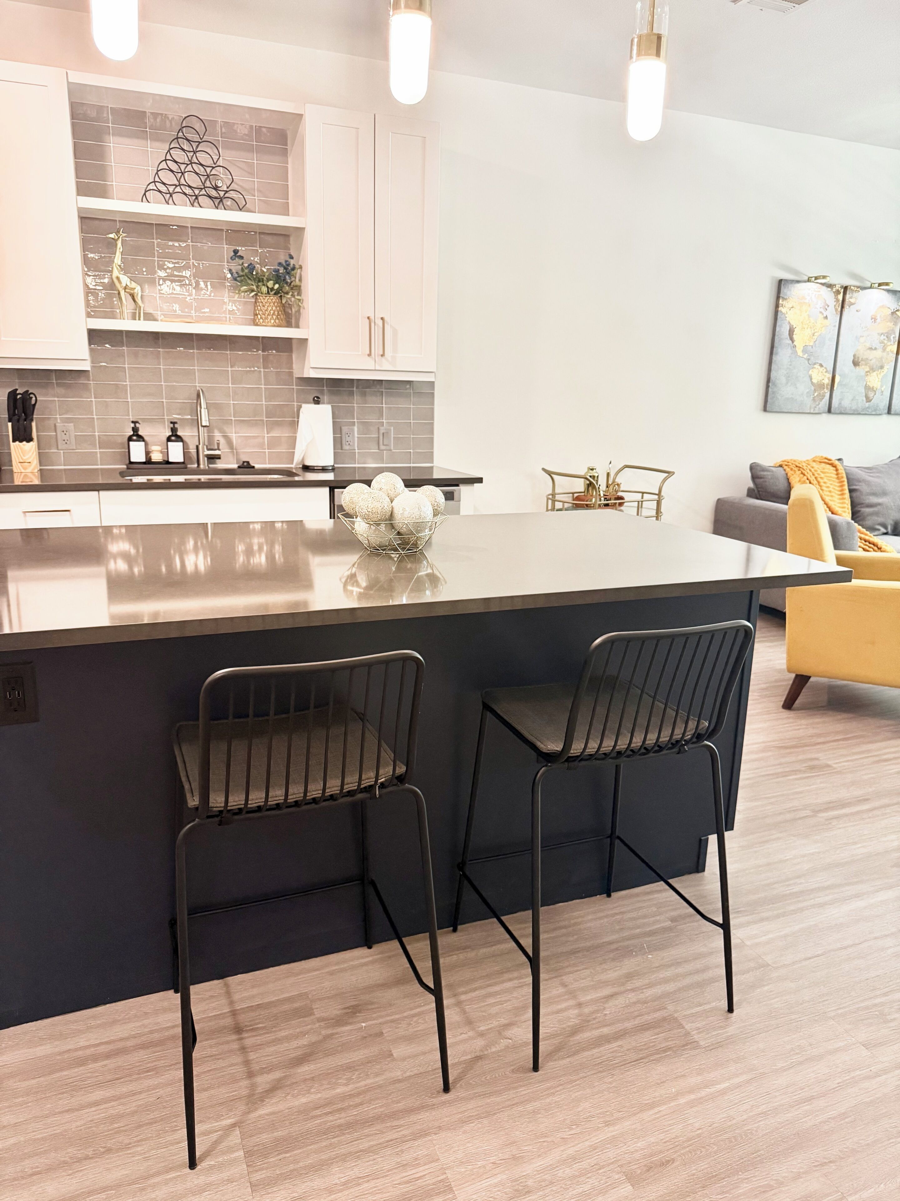 Una cocina moderna con una isla central, dos taburetes de bar y un comedor con un sofá y una mesa de centro.