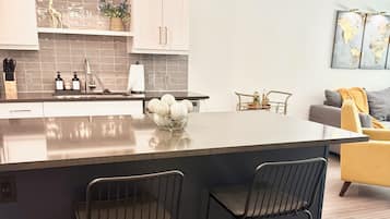 Una cocina moderna con una isla central, dos taburetes de bar y un comedor con un sofá y una mesa de centro.