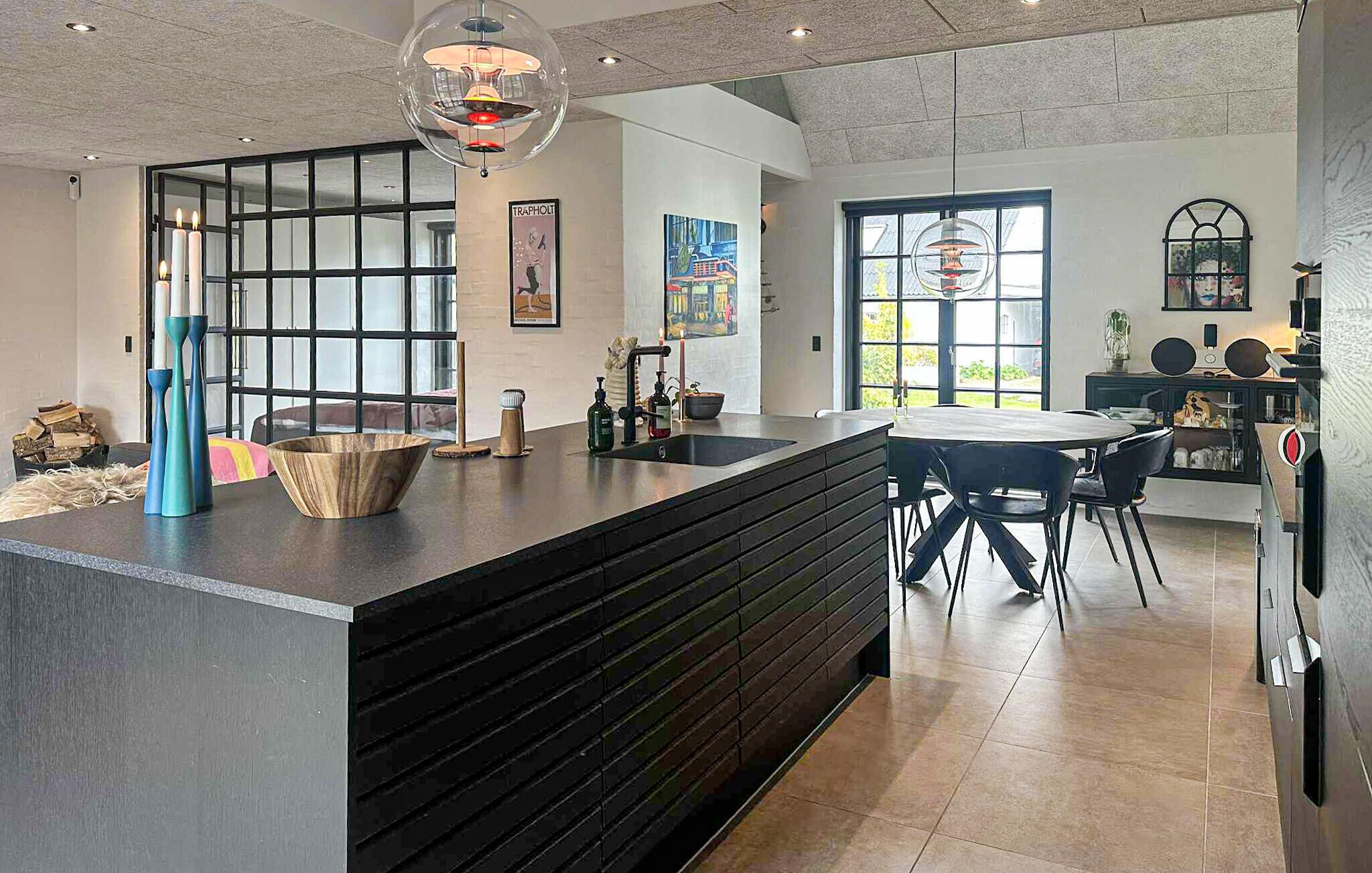 A modern kitchen with a central island, a dining area with a round table, and a large window providing natural light.