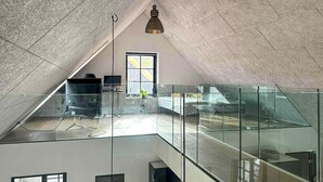 Een modern loft met glazen balustrade, een hanglamp en uitzicht buiten.
