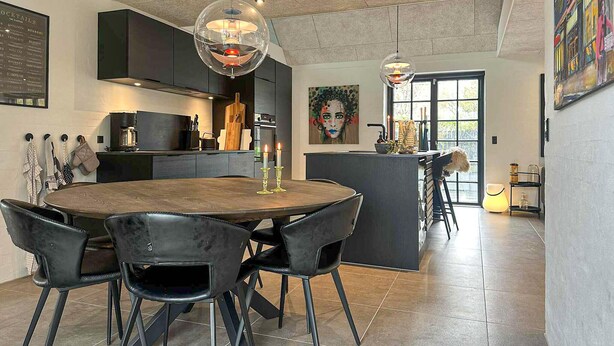 Een moderne keuken met een eethoek, met een ronde tafel, zwarte stoelen, hanglampen en een schilderij aan de muur.