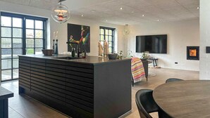 Een moderne keuken met een centraal kookeiland, grote ramen, een flatscreen televisie en een open haard.