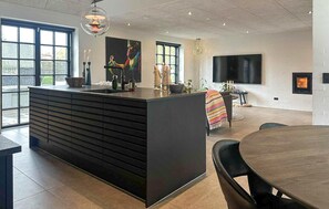 A modern kitchen with a central island, large windows, a flat-screen TV, and a fireplace. - Gorgeous home in Samsø with WiFi (Samsø)
