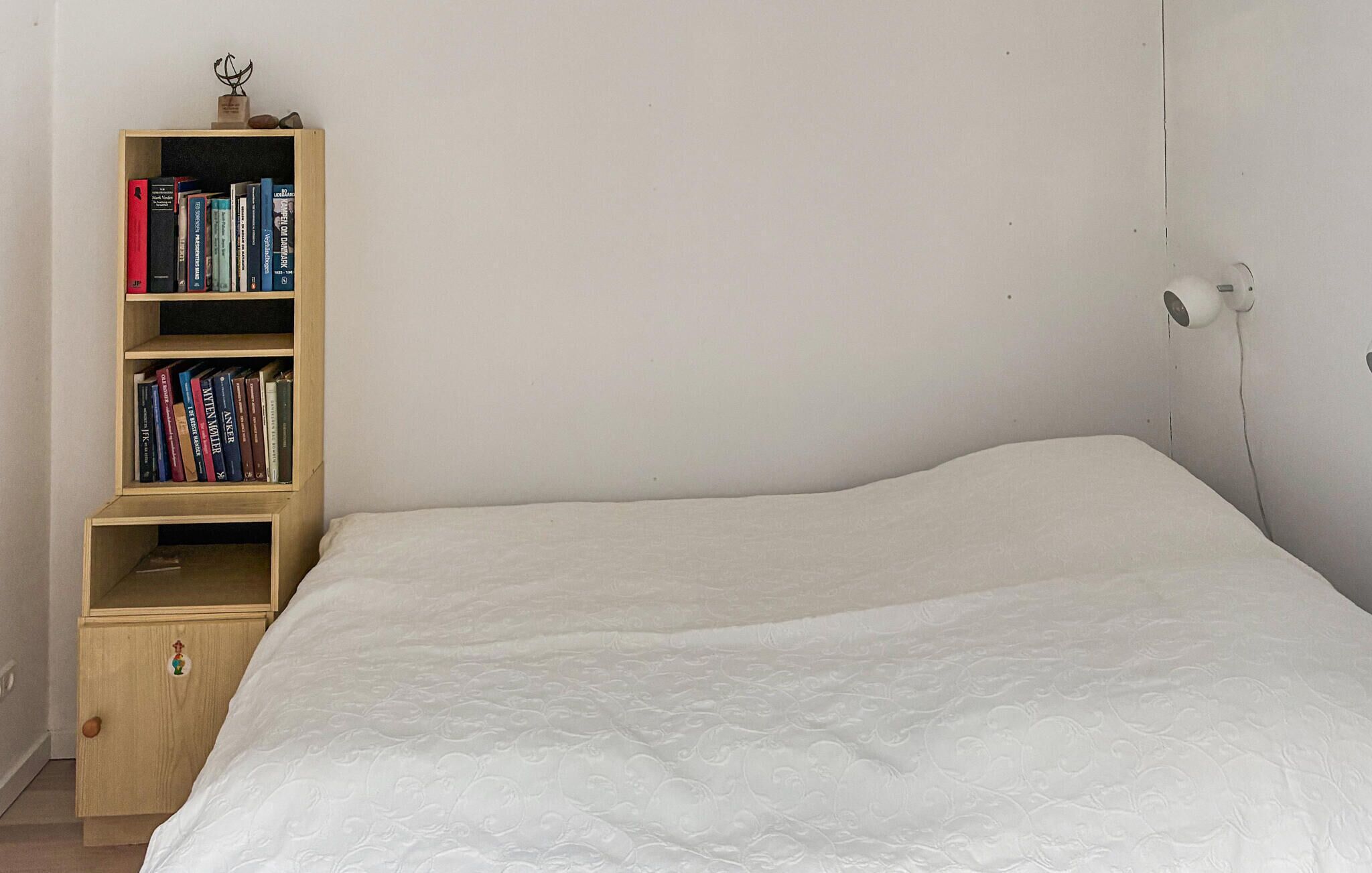 Une chambre avec un lit simple, une bibliothèque en bois et une prise électrique au mur.