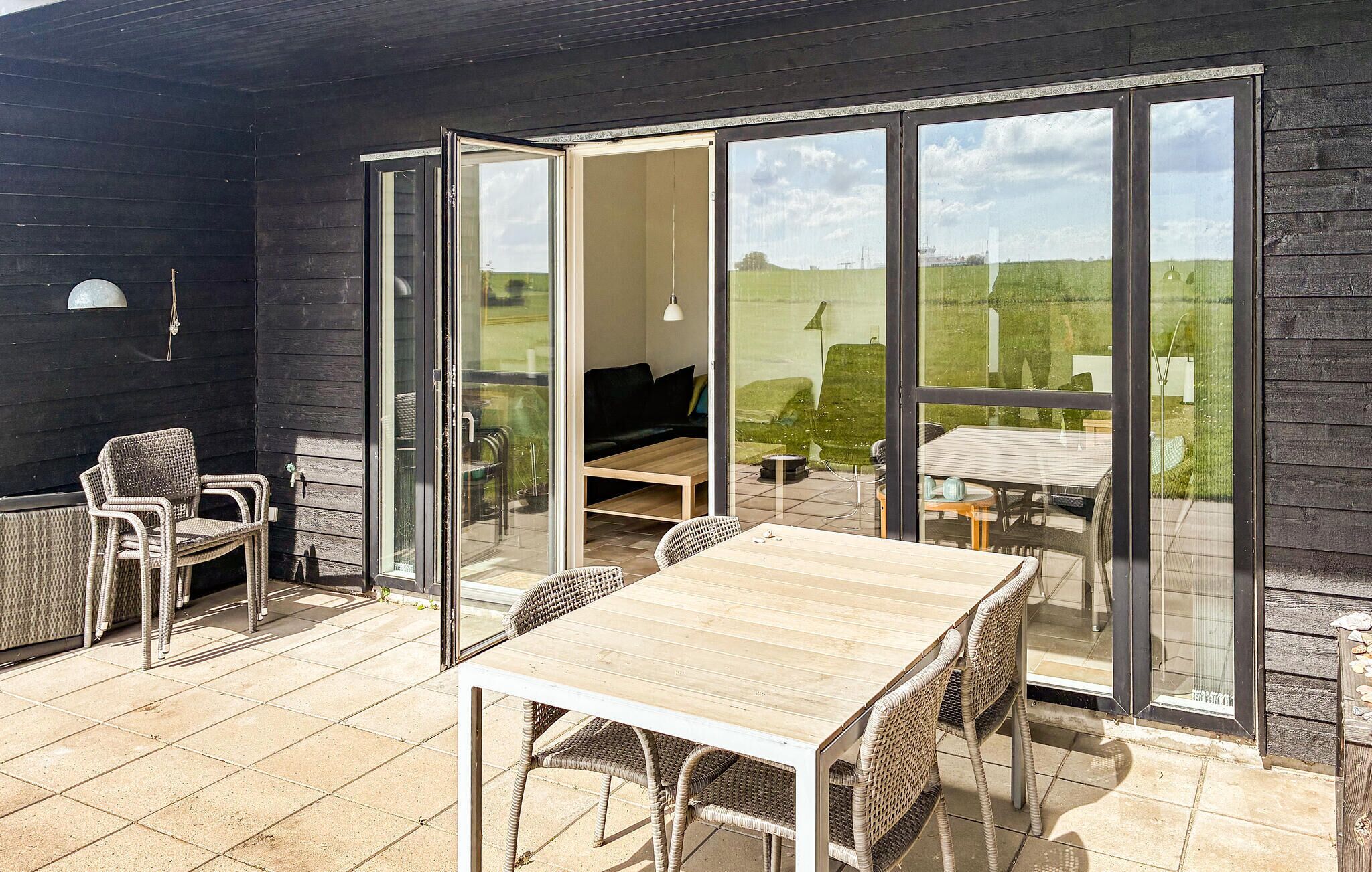 Eine Terrasse im Freien mit Tisch und Stühlen, einer Sitzecke und einer Glasschiebetür, die in einen Garten führt.