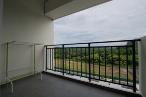 A balcony with a metal railing, a drying rack, and a view of greenery and a road.