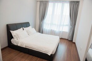 A neatly made bed in a room with wooden flooring and a large window with curtains.