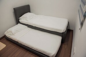 A twin bed with a headboard, a single bed with a headboard, and a wooden floor.