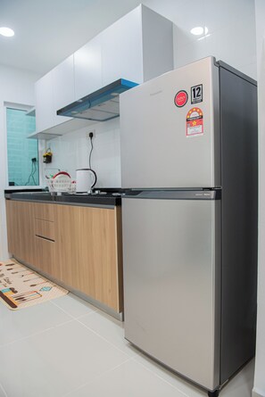 A kitchen with a stainless steel refrigerator, wooden cabinets, a black countertop, and a white tiled backsplash.