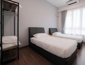 Hotellihuone, jossa on kaksi sänkyä, vaatekaappi, ilmastointilaite ja ikkuna, jossa on verhot.