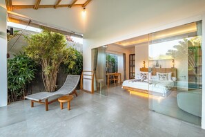 Une chambre moderne avec un mur en verre, un lit avec une literie blanche, une petite table et une chaise.
