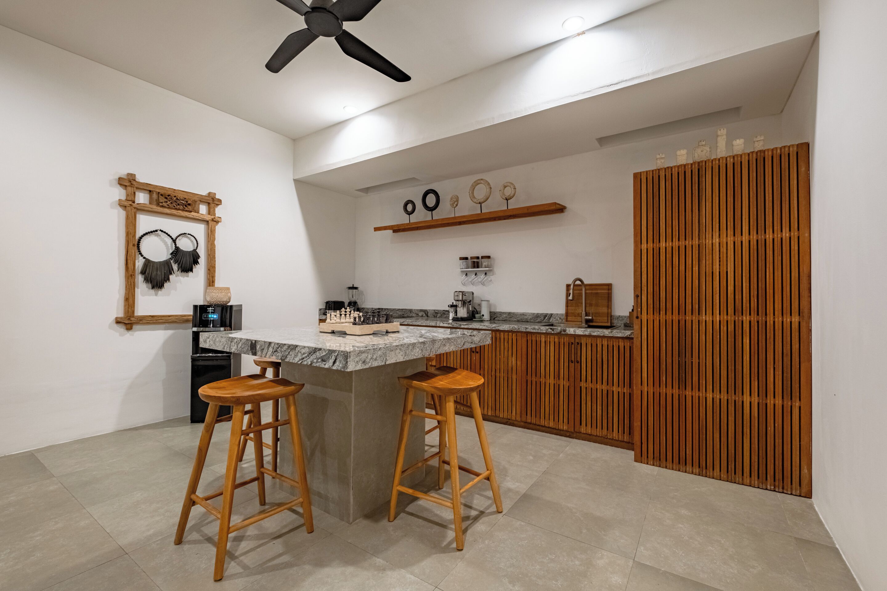 Una cocina con taburetes de madera, ventilador de techo, encimera de mármol y un mueble de madera.