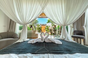 Una habitación con cama, cortinas blancas, vistas a zonas verdes y una disposición de toallas en forma de corazón.