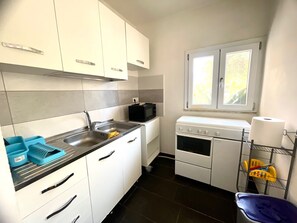 Een kleine keuken met witte kastjes, een roestvrijstalen spoelbak, een magnetron, een fornuis en een raam met uitzicht.