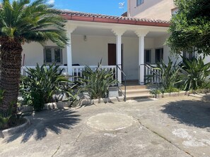 A building with a covered porch, white columns, and potted plants.