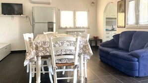 Un espace repas comprenant une table et des chaises, un canapé bleu, un téléviseur et un coin cuisine avec un réfrigérateur et une cuisinière.