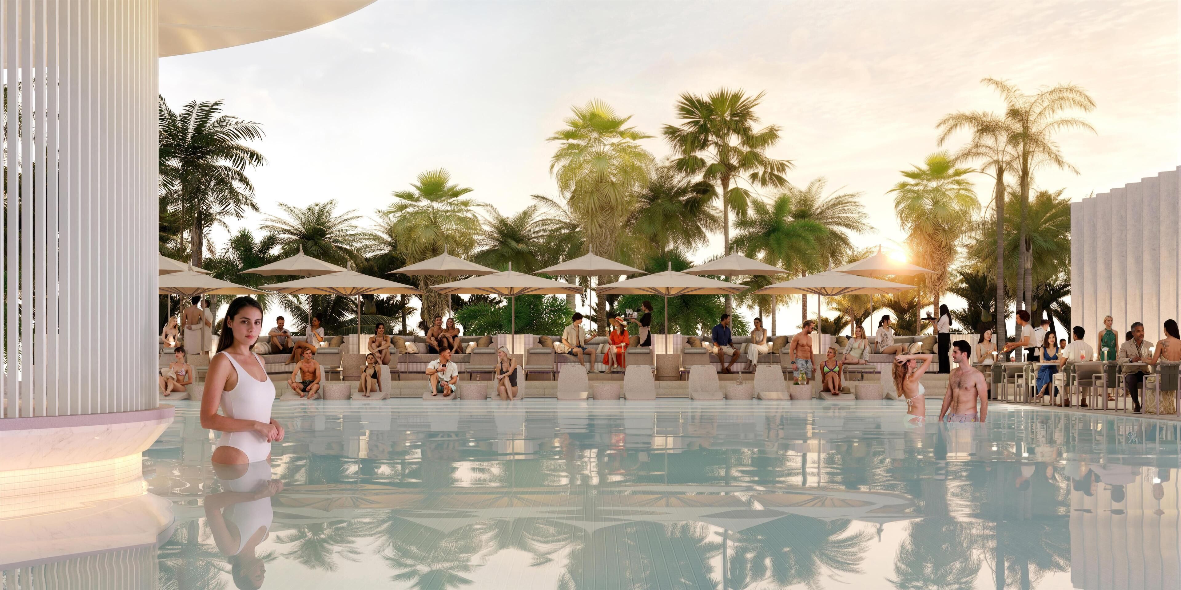 Un área junto a la piscina con sillones de descanso y sombrillas, rodeada de palmeras.
