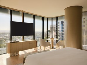 A hotel room with a large bed, a desk with a chair, a small table with two chairs, a TV, and a view of a cityscape through large windows. - Andaz Gold Coast by Hyatt (GOLD COAST)