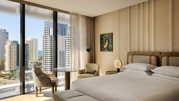 A hotel room with a large bed, a seating area with a table, and a view of city buildings.