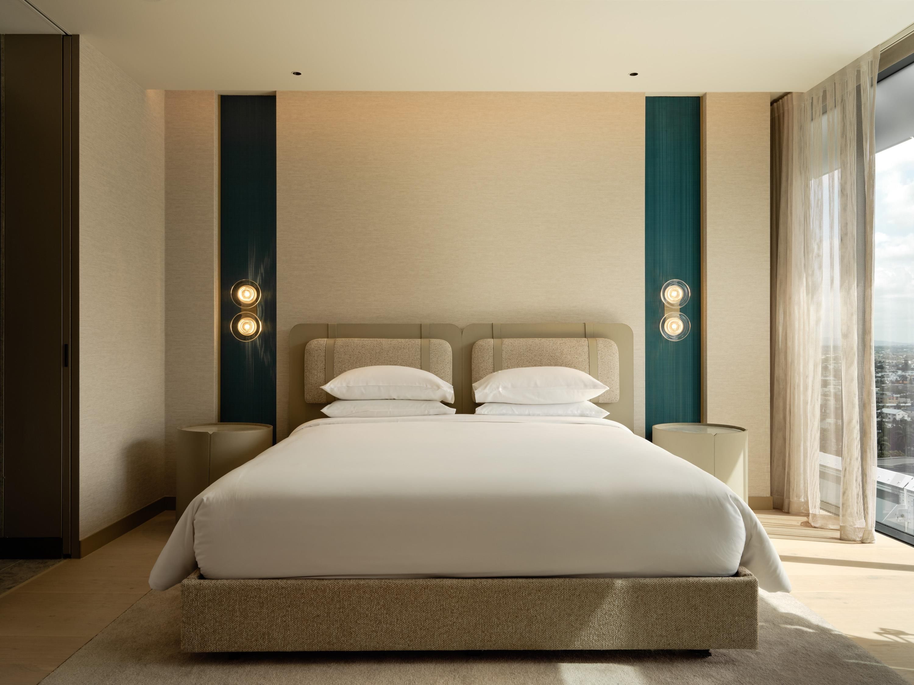 Une chambre d’hôtel moderne avec un grand lit, deux tables de chevet et une vue sur la ville.