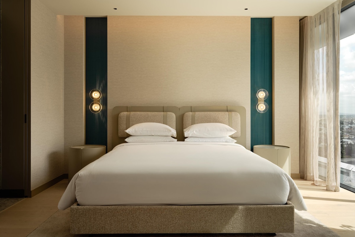 Habitación de hotel moderna con una cama grande, dos mesitas de noche y vistas a la ciudad.