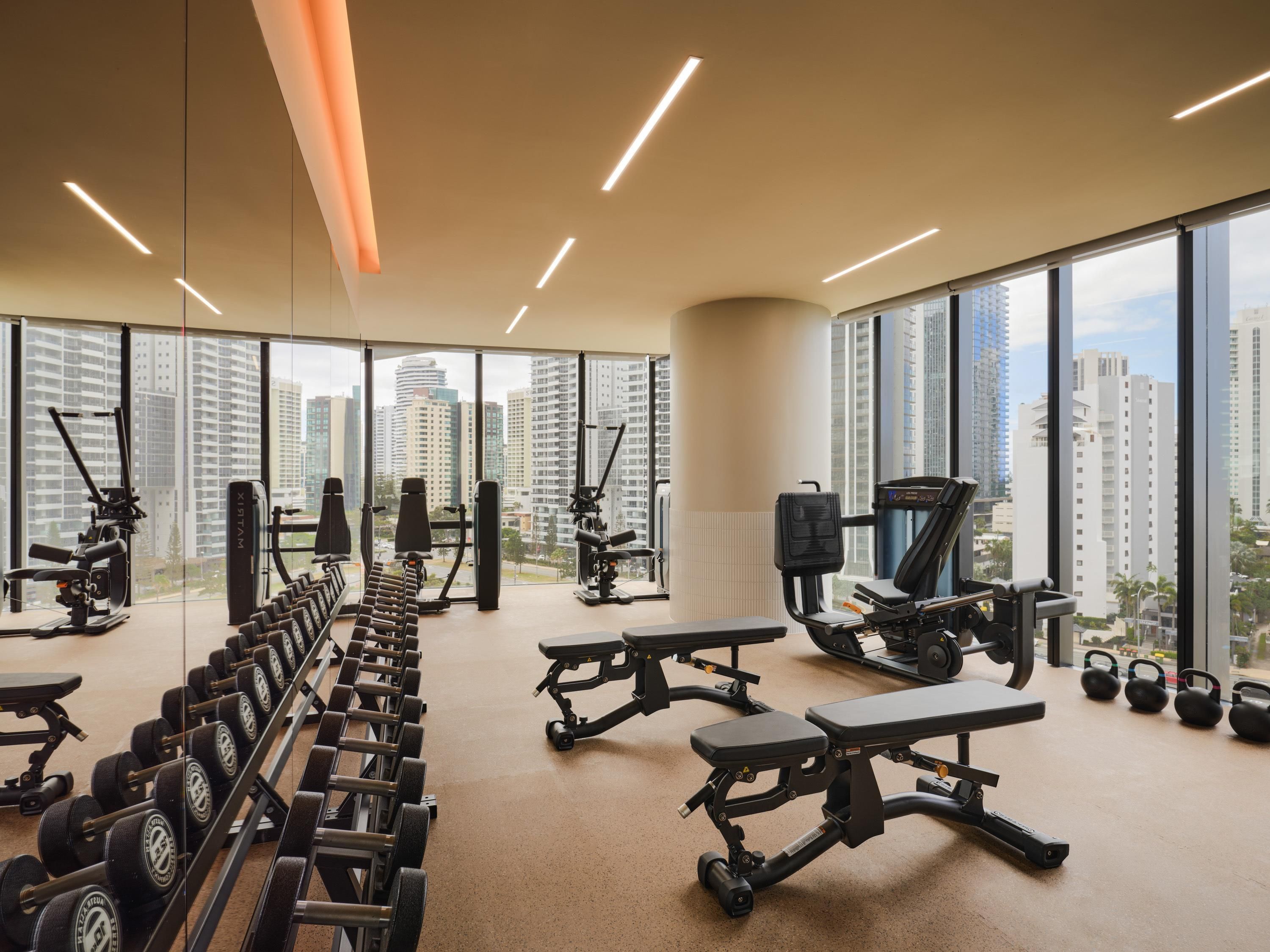 A gym with exercise equipment, large windows, and a city view.