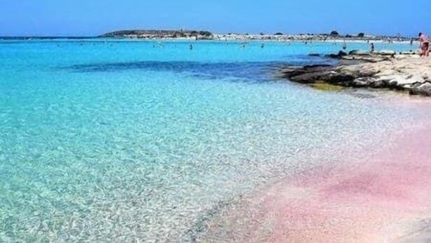 A beach with clear turquoise water, rocky shoreline, and distant buildings. - Western Sun near Balos & Falassarna (Trachilos)