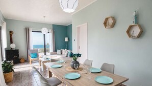 A dining area with a wooden table set for four, grey chairs, and a view of the sea through the glass door. - Western Sun near Balos & Falassarna (Trachilos)