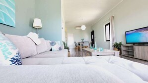 A modern living room with a sofa, a flat-screen TV, a dining area, and a kitchen visible in the background. - Western Sun near Balos & Falassarna (Trachilos)
