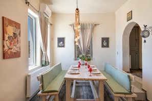 A dining area with a wooden table set for four, benches with cushions, a hanging light fixture, and framed pictures on the walls. - Villa Fotis Country House with Sea View, Wi-Fi, and Air Conditioning (Megas Gialos)