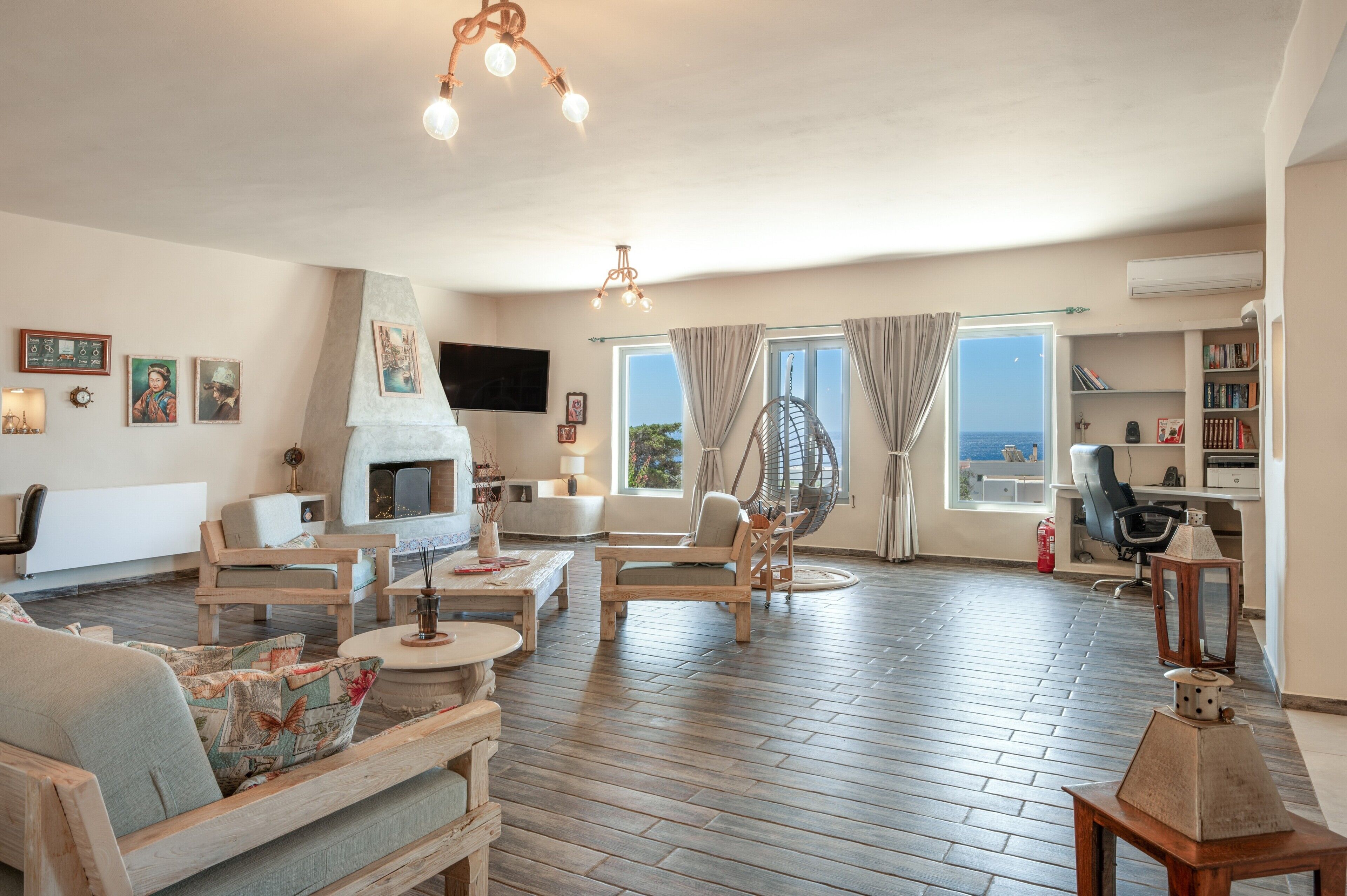 A spacious living room with a fireplace, wooden furniture, a large window with a view, and a bookshelf.