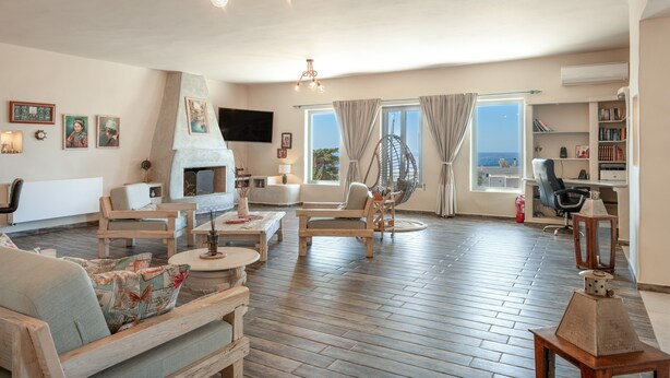 A spacious living room with a fireplace, wooden furniture, a large window with a view, and a bookshelf. - Villa Fotis Country House with Sea View, Wi-Fi, and Air Conditioning (Megas Gialos)