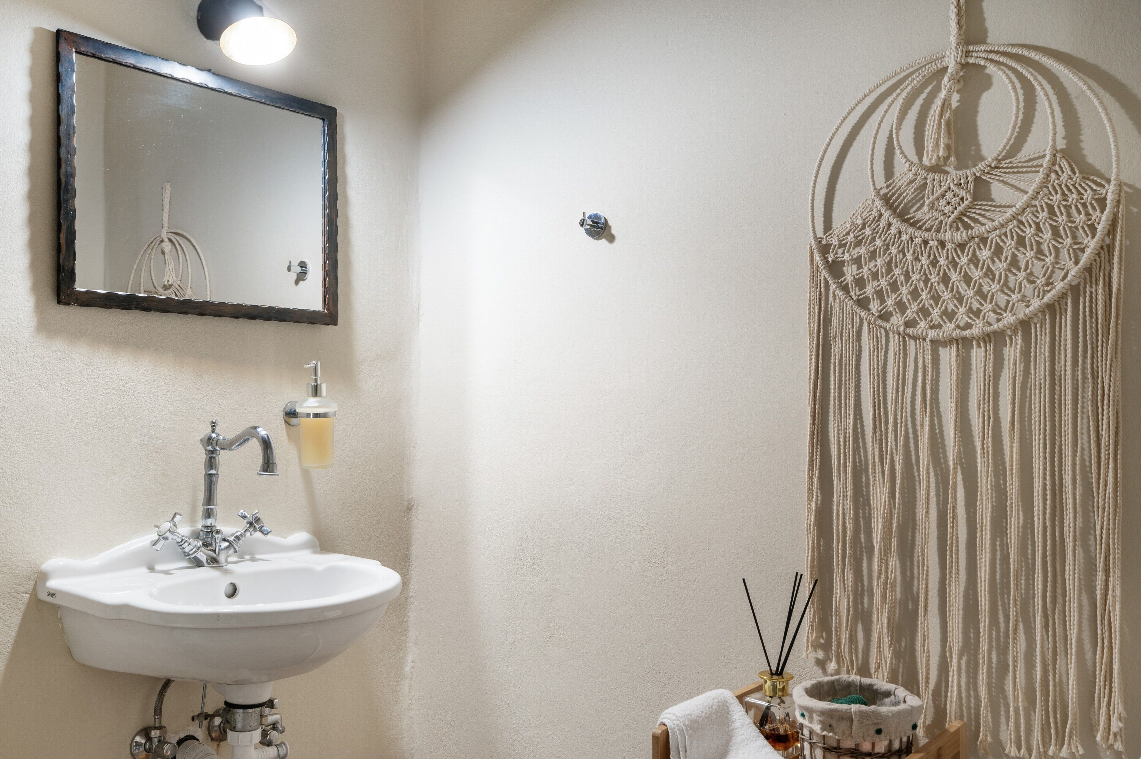 Ein Badezimmer mit einem weißen Waschbecken, einem Spiegel und einer Wanddekoration aus Makramee.