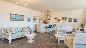 A living room with a sofa, coffee table, and chairs, a kitchen area with a bar, and various wall decorations. - Villa Fotis Country House with Sea View, Wi-Fi, and Air Conditioning (Megas Gialos)