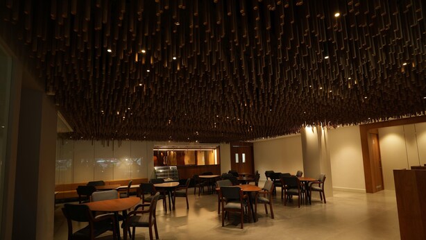 A modern interior with a unique ceiling design, seating arrangements, and a glass partition. - Ramada Encore by Wyndham Kochi Kalamassery (Kanayannur)