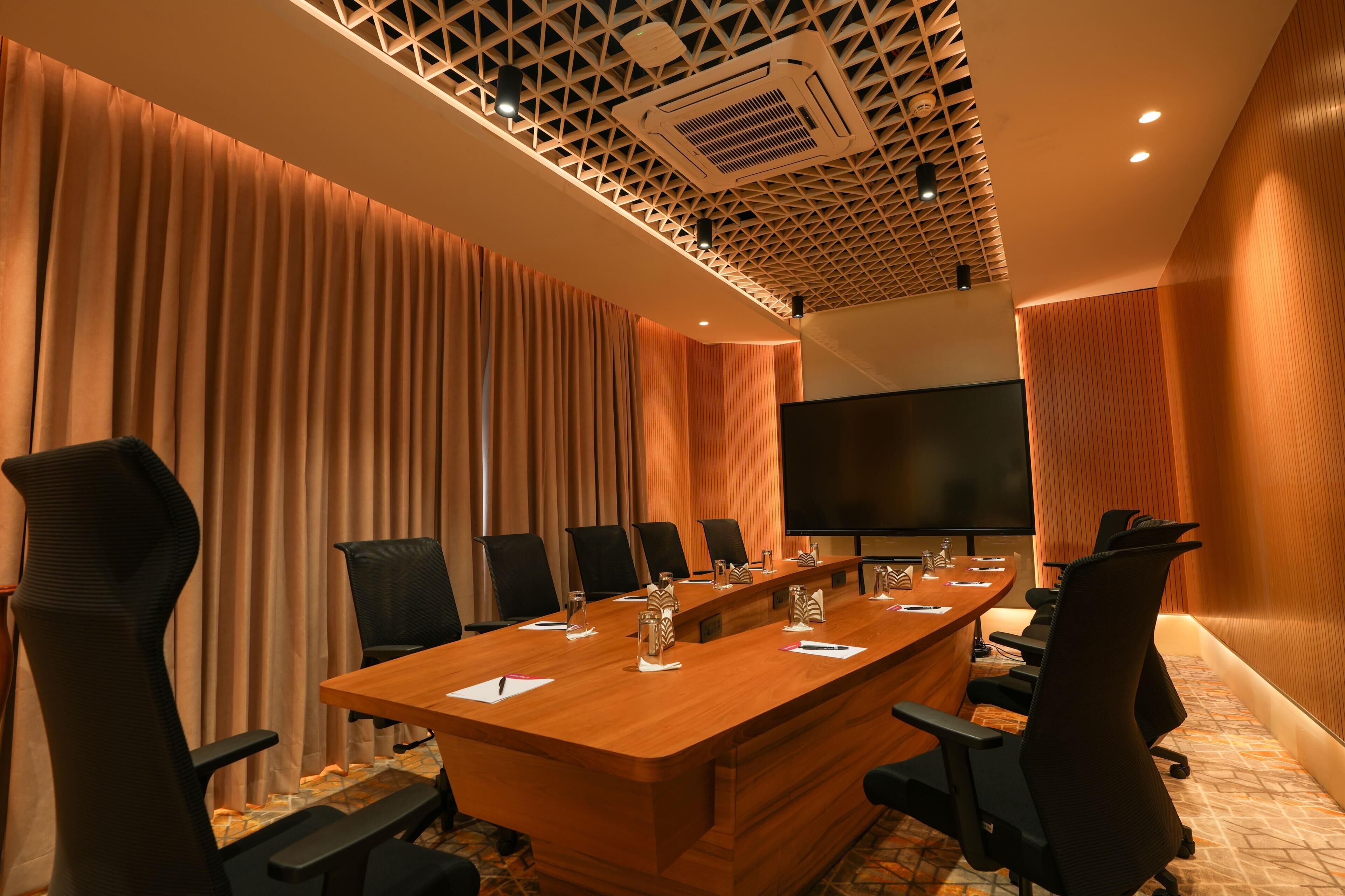 A conference room with a long table, black chairs, a large screen, and a patterned ceiling.
