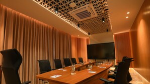A conference room with a long table, black chairs, a large screen, and a patterned ceiling. - Ramada Encore by Wyndham Kochi Kalamassery (Kanayannur)