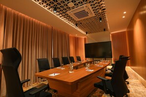 A conference room with a long table, black chairs, a large screen, and a patterned ceiling.