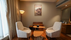 A hotel room with two armchairs, a small wooden table, a sofa, a painting on the wall, and a kitchenette area. - Ramada Encore by Wyndham Kochi Kalamassery (Kanayannur)