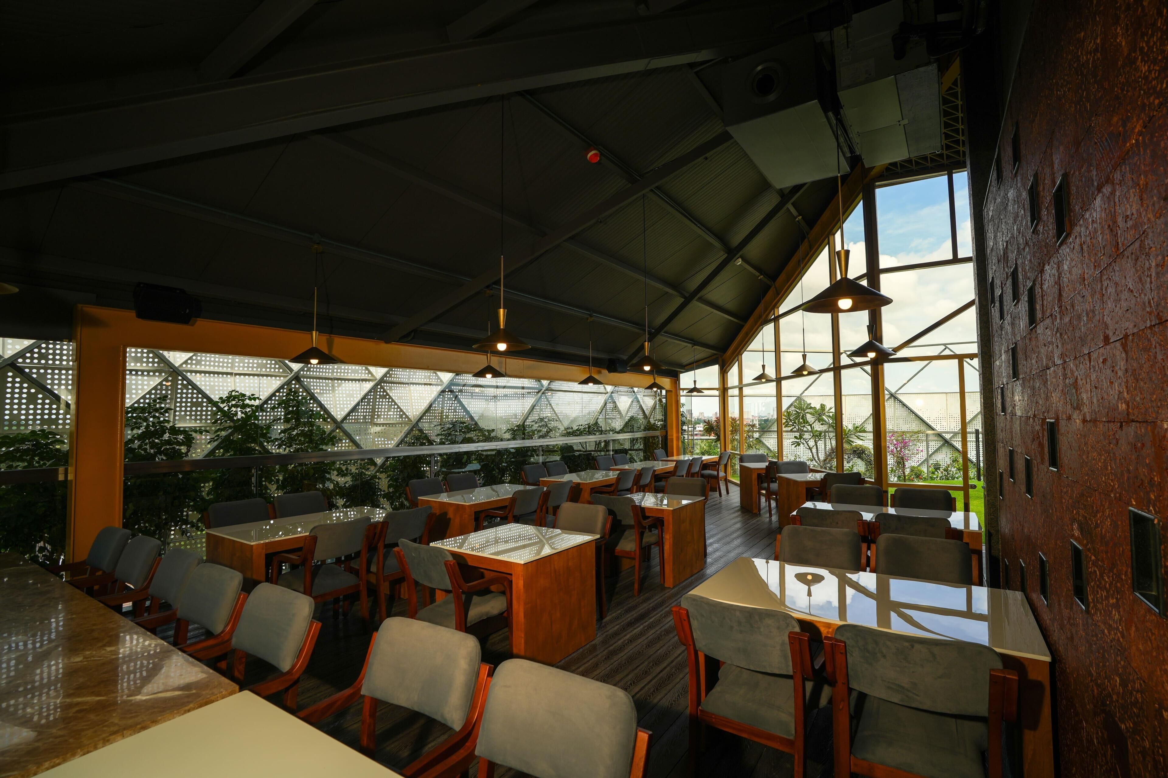 Un comedor interior con mesas, sillas, ventanas amplias y lámparas colgantes.